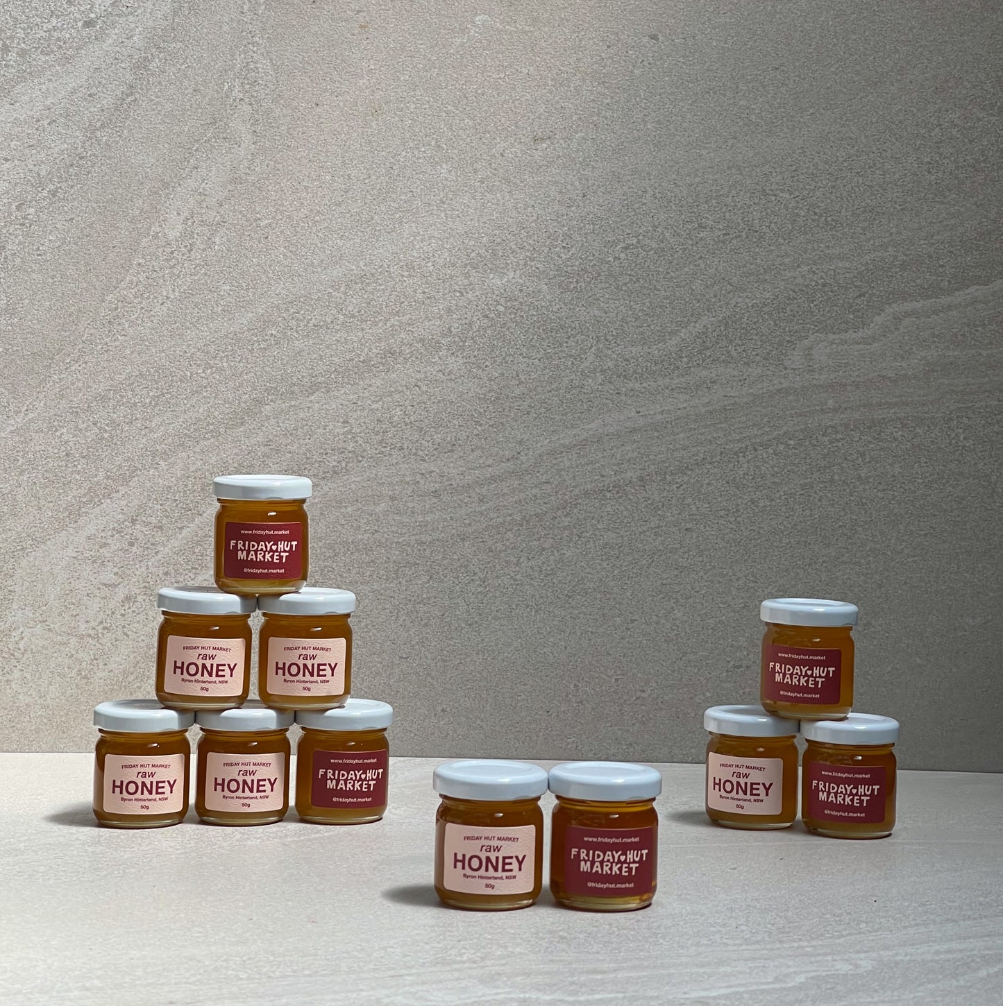 50g jars of Friday Hut Market Raw bush Honey are stacked on top of each other in a pyramid.