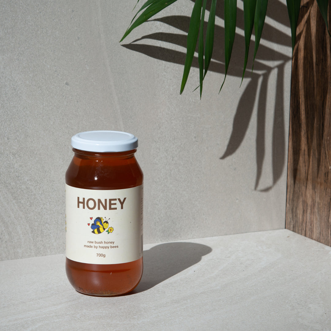 A 700g jar of Friday Hut Market Raw Bush Honey sits with a leaf in the background.