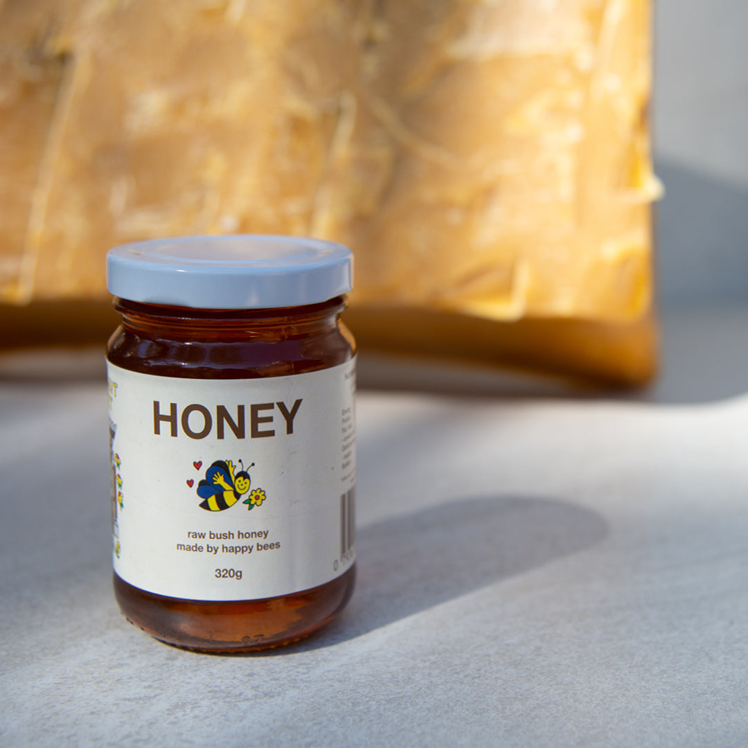 a 320g jar of Friday Hut Market Raw Bush Honey sits in front of a large block of golden beeswax.