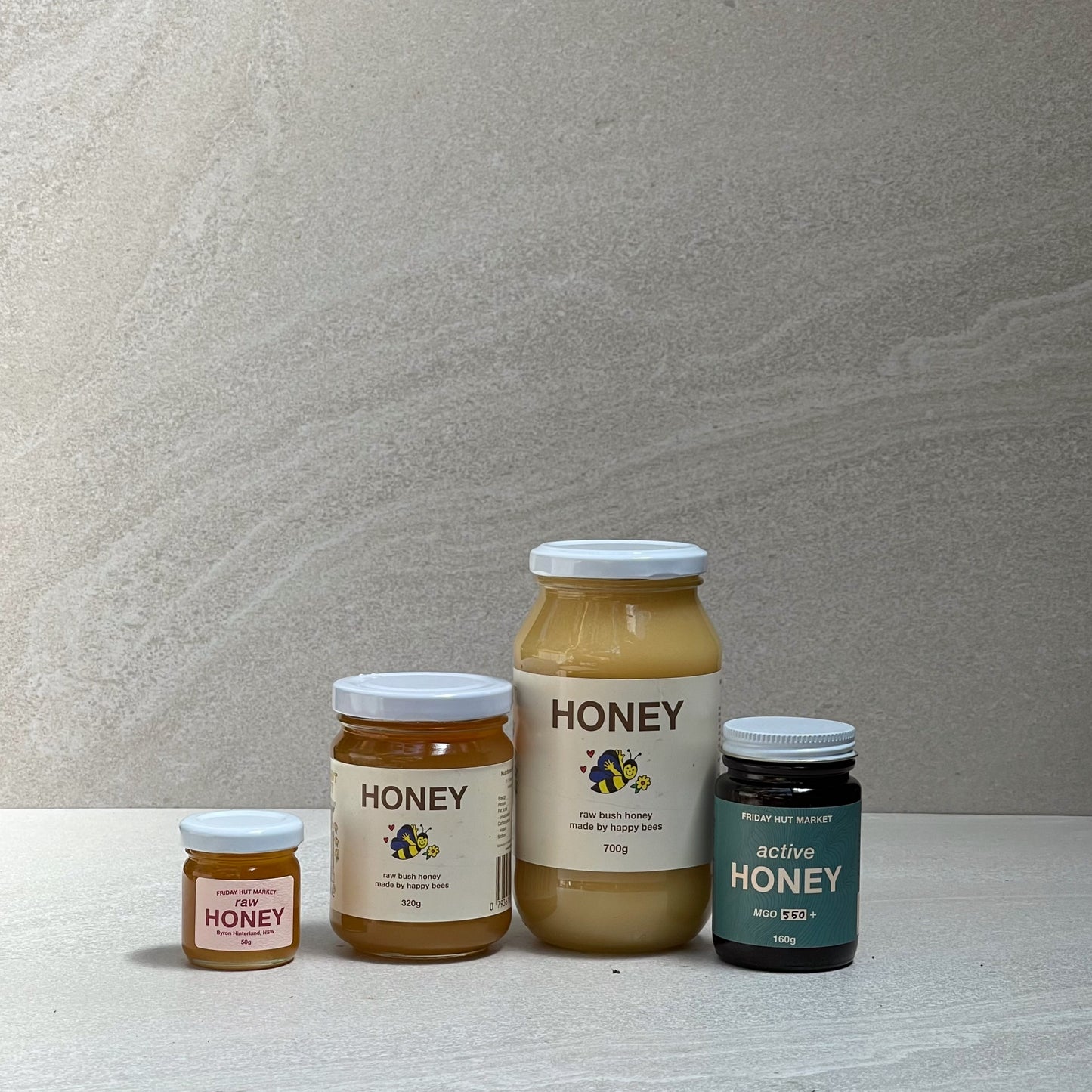 A collection of 50g, 320g and 700g jars of Friday Hut Market Raw Bush Honey sit alongside a jar of MGO 550+ Active Jellybush Manuka Honey.